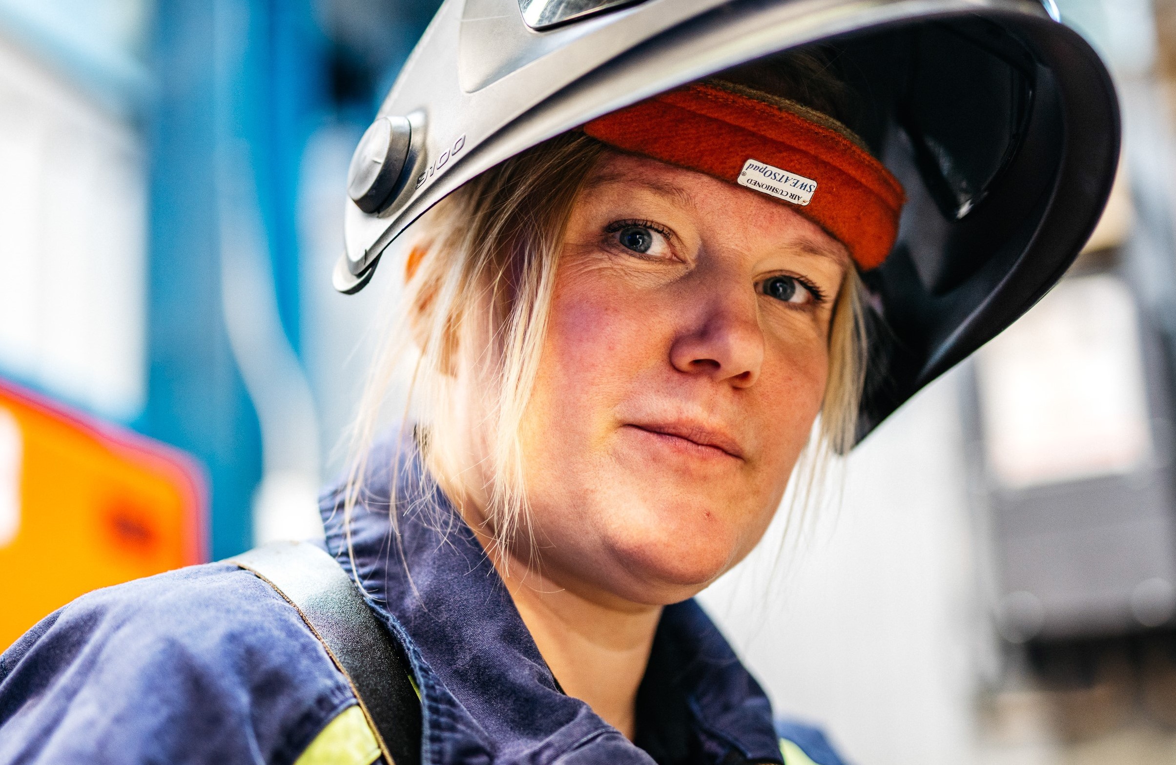 En person bär skyddsutrustning, inklusive hjälm och arbetskläder, i en industriell miljö.