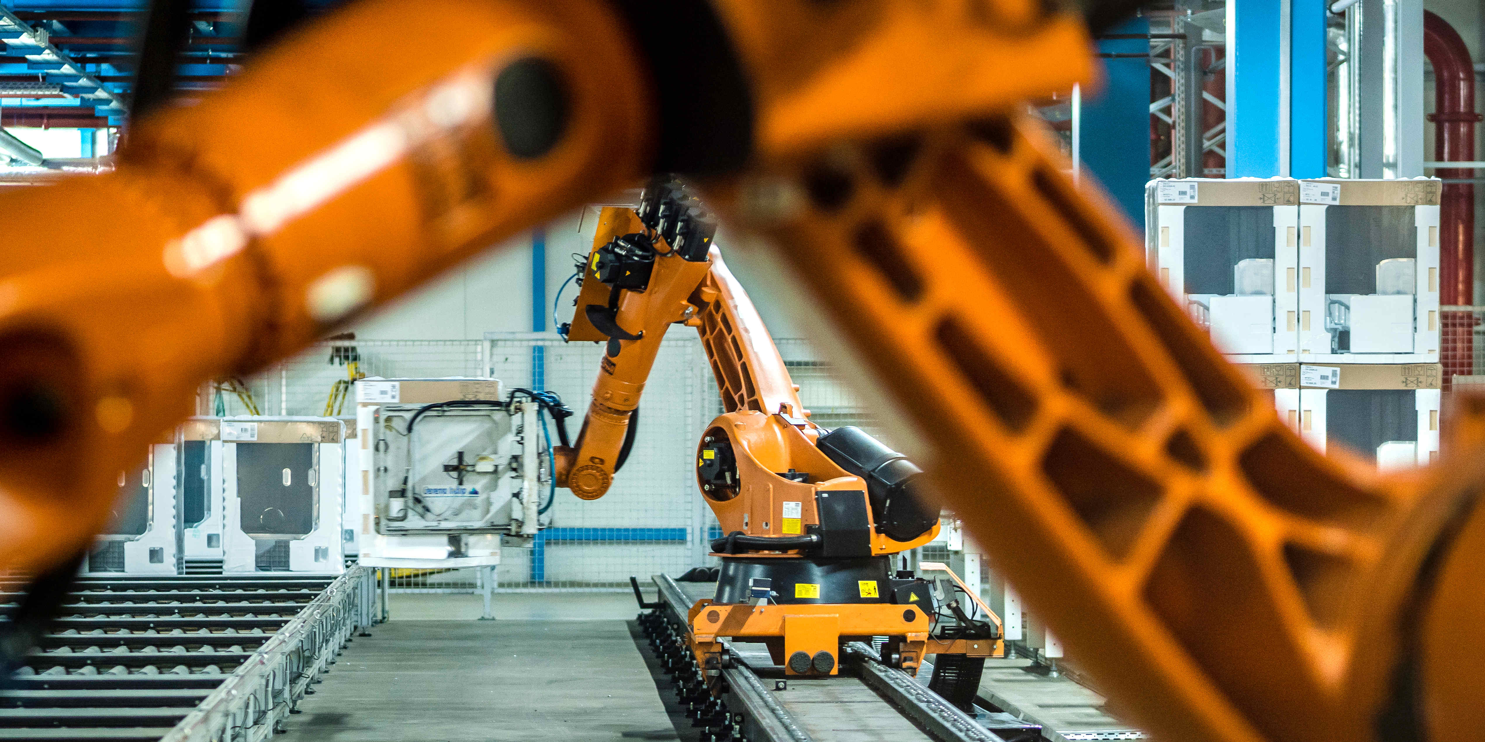 Flera orange industrirobotar arbetar längs en automatiserad produktionslinje i en modern fabrik med metallstrukturer, skyddspaneler och stark belysning.