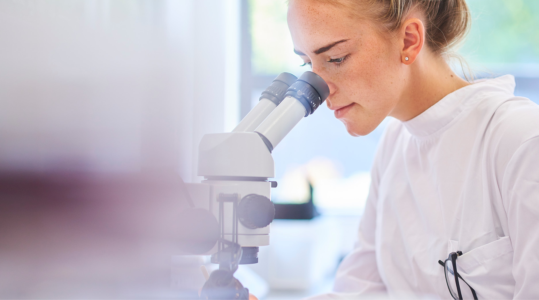 En person arbetar vid ett mikroskop i en laboratoriemiljö, med fokus på analysarbete vid ett labbbord.