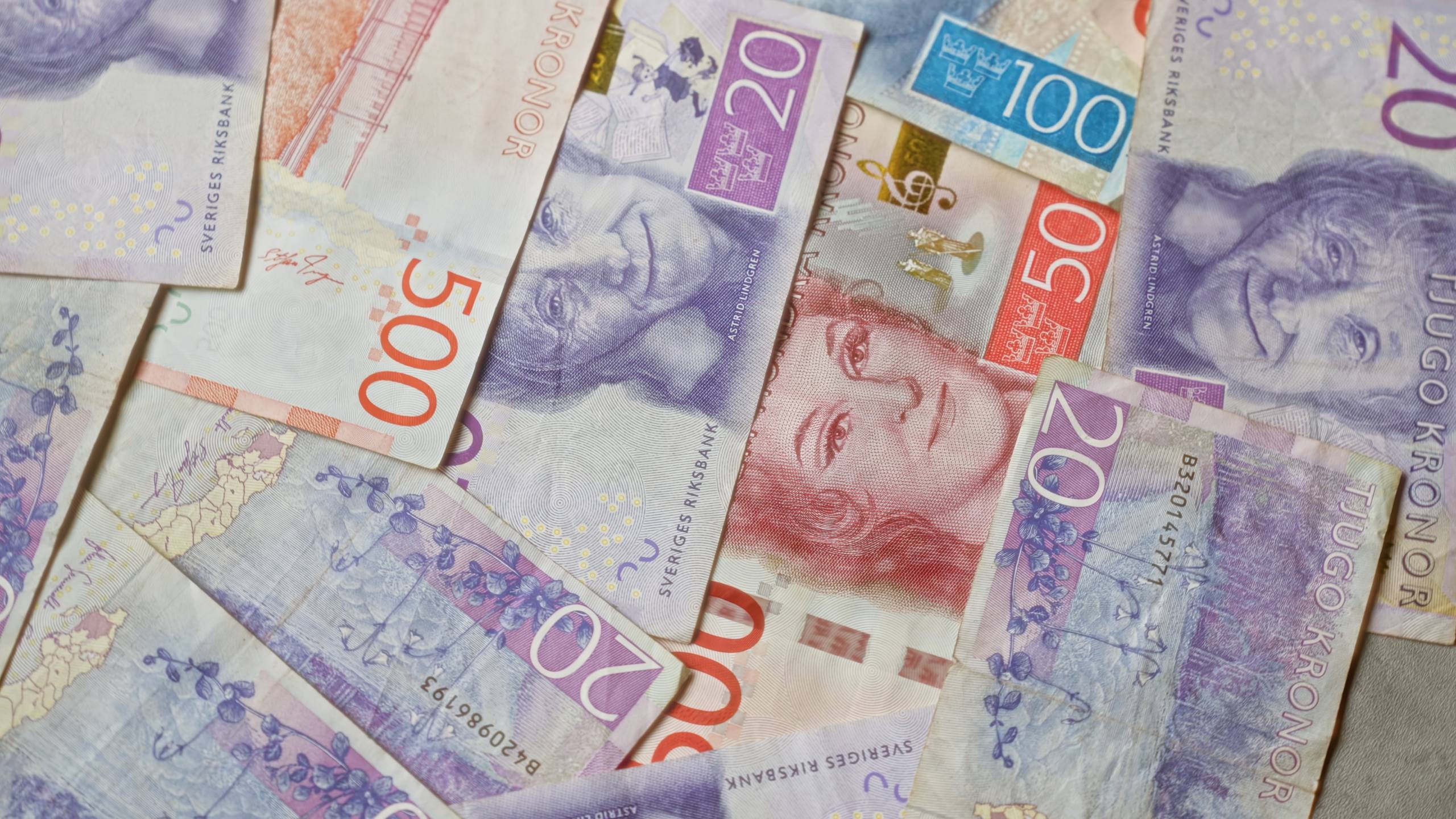 Mehrere schwedische Banknoten in verschiedenen Stückelungen (20, 50, 100, 200 und 500 Kronen) liegen verstreut und überlappen sich.