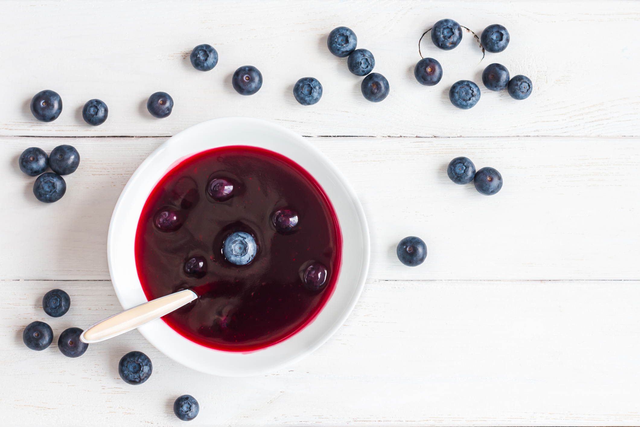 Schale mit schwedischer Blaubeersuppe auf einem weißen Tisch, umgeben von frischen Blaubeeren.