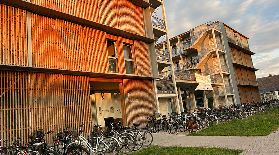 Flerbostadshus med träfasad i kvällssol och många parkerade cyklar framför.