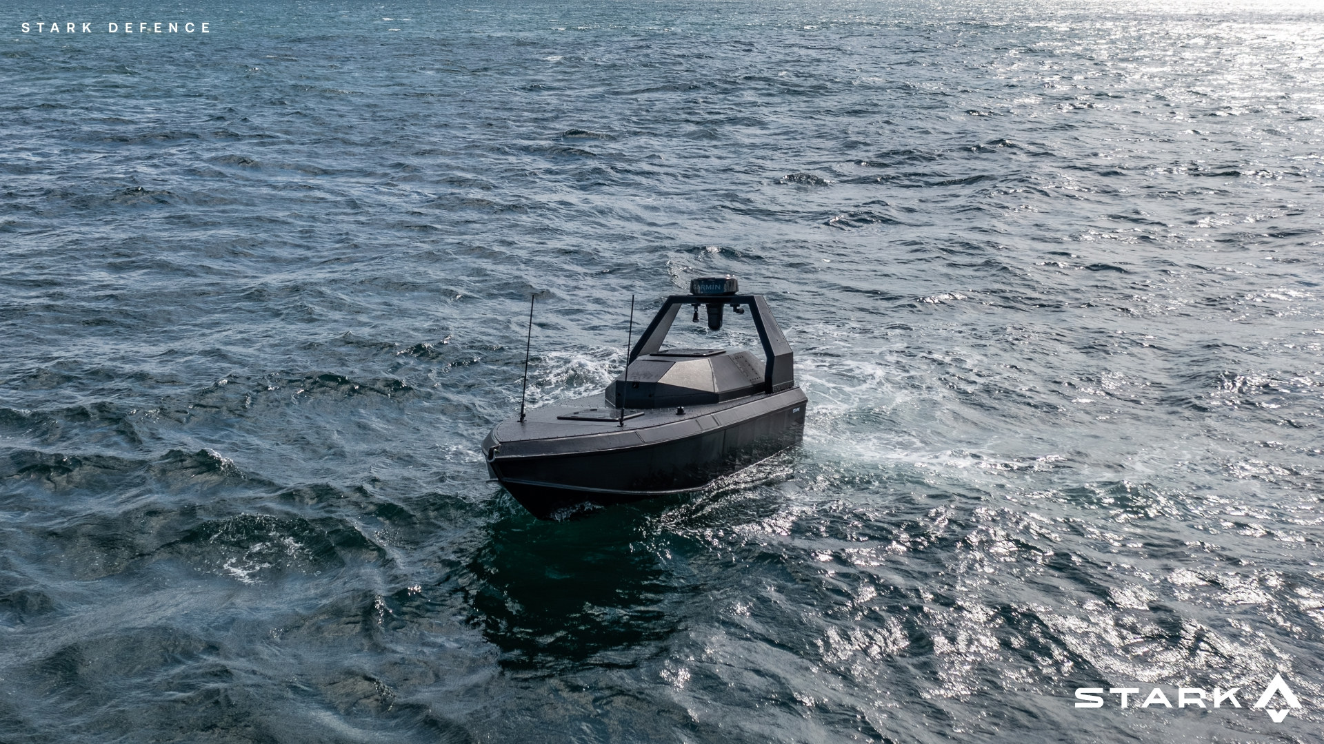 Ein unbemanntes, dunkel gefärbtes Wasserfahrzeug bewegt sich über eine leicht wellige Meeresoberfläche, mit weit ausgedehntem Wasser unter klarem Himmel.