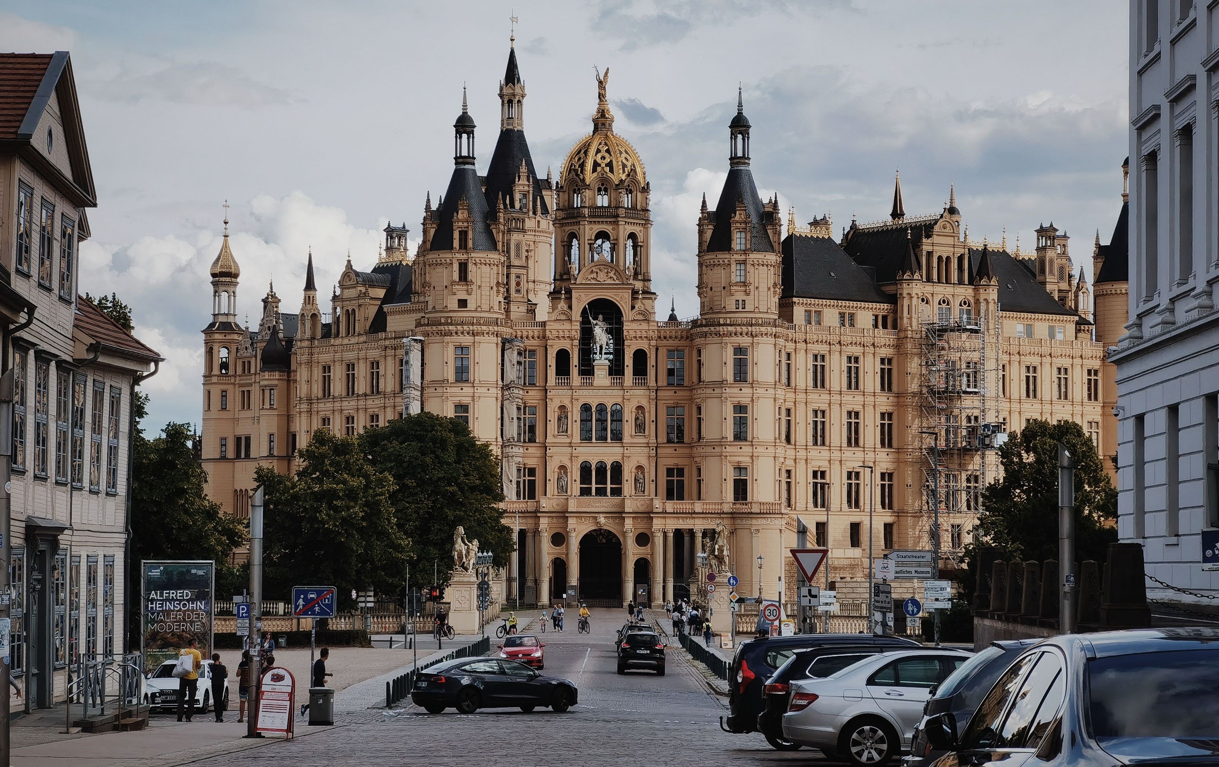 Schwerins slott i ett panorama mot en molnig himmel med livlig aktivitet i förgrunden.