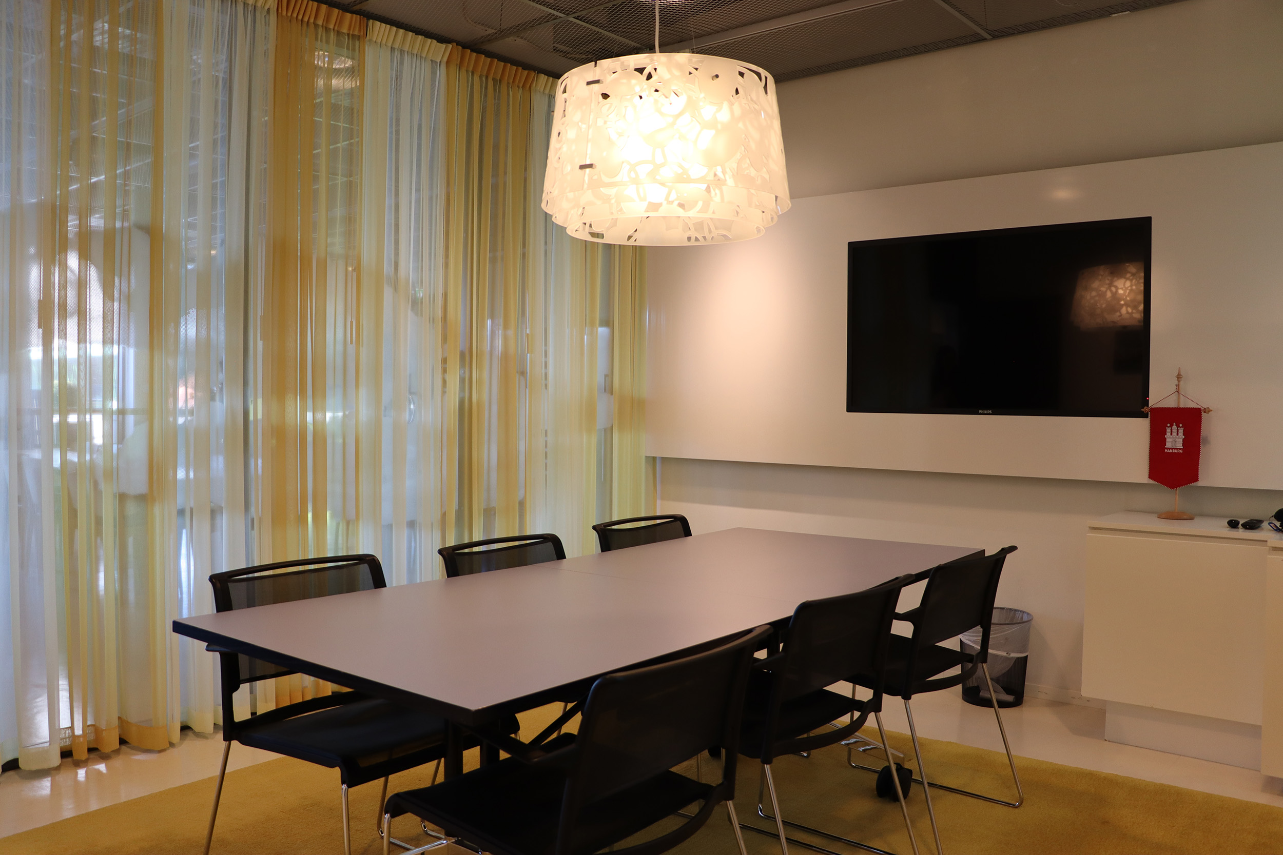 Konferenzraum in der Deutsch-Schwedischen Handelskammer mit Tisch und sechs Stühlen, wandmontiertem Fernseher und großen Fenstern mit hellen Vorhängen.