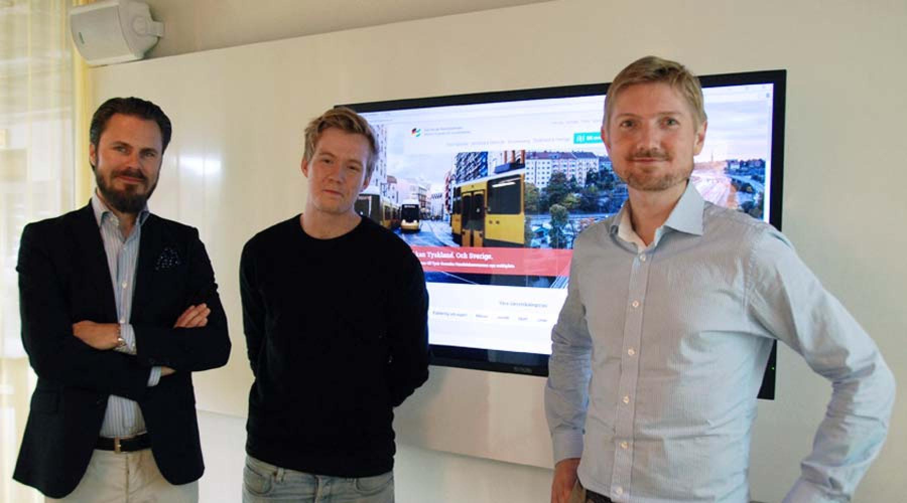 Thomas Alsén, Marcus Tisäter und Stefan Hamilton von Happiness stehen vor einem Fernsehbildschirm, auf dem die neue Webseite der Deutsch-Schwedischen Handelskammer zu sehen ist.