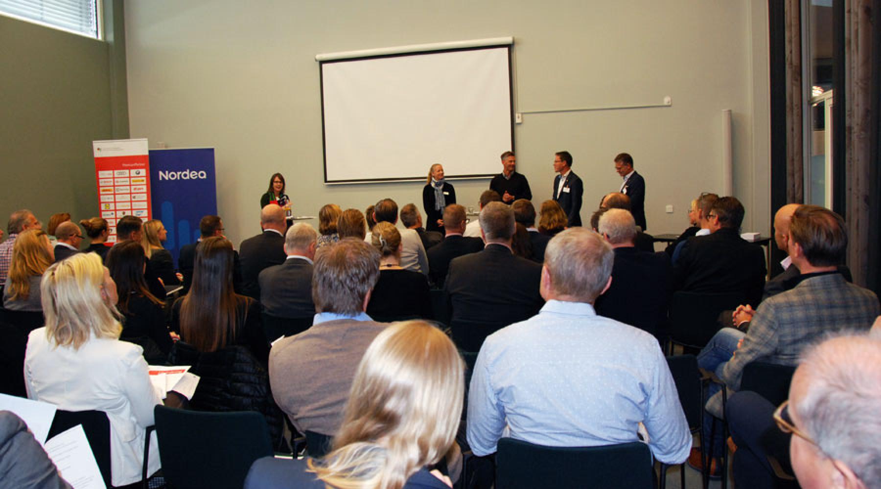 Ett fullsattseminarierum: Publiken syns i förgrunden, panelen och moderatorn i bakgrunden.