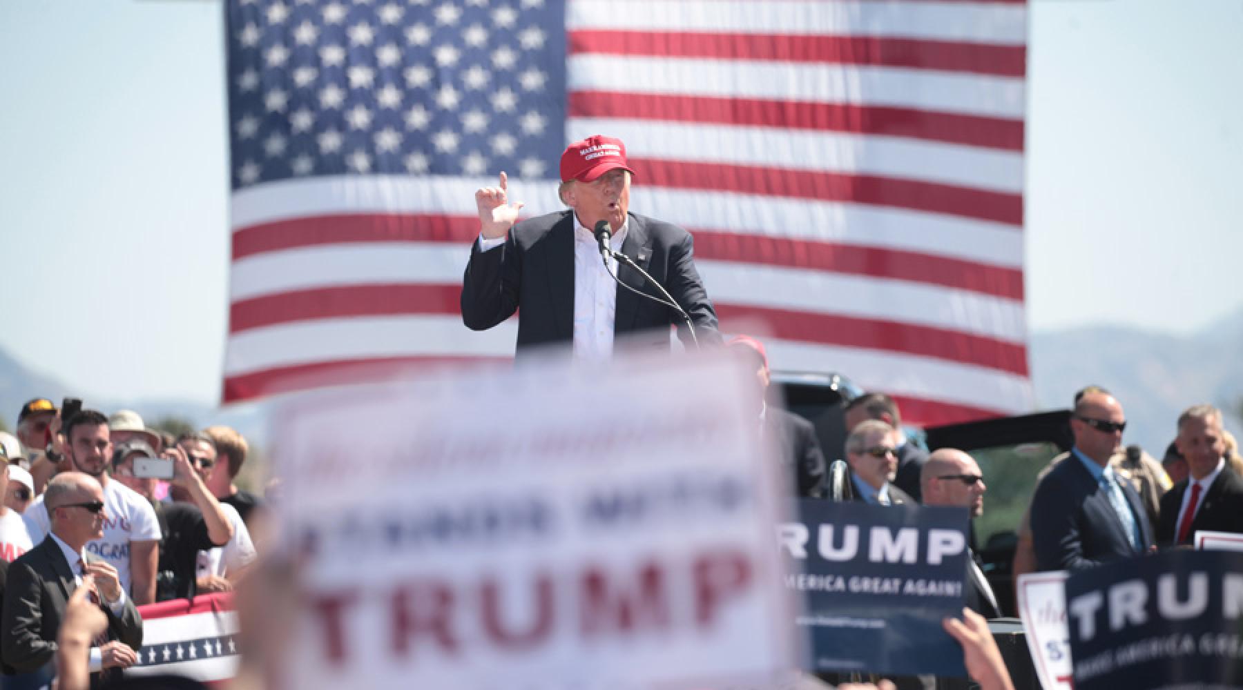 Donald Trump auf einer Wahlkampfveranstaltung. Im Publikum halten zahlreiche Menschen Schilder mit seinem Namen in die Höhe.