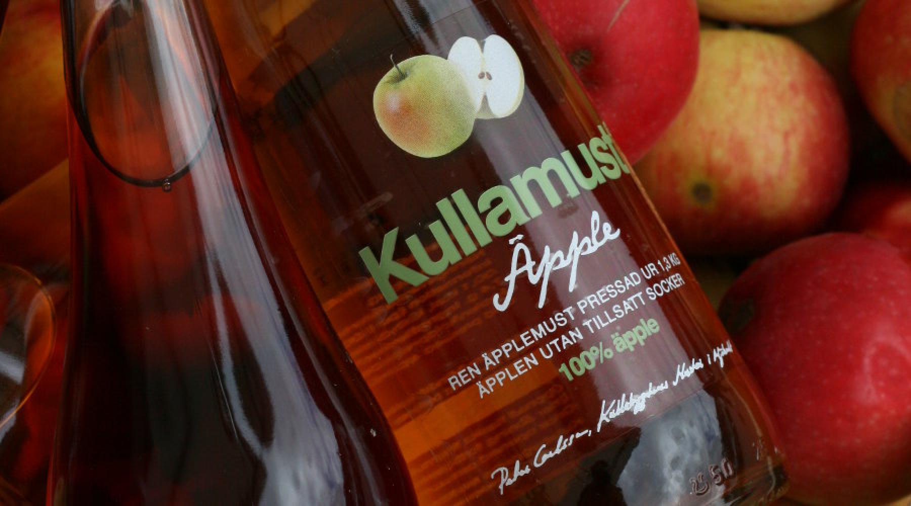 Kullabygdens Kullamust in einer Flasche und Äpfel im Hintergrund