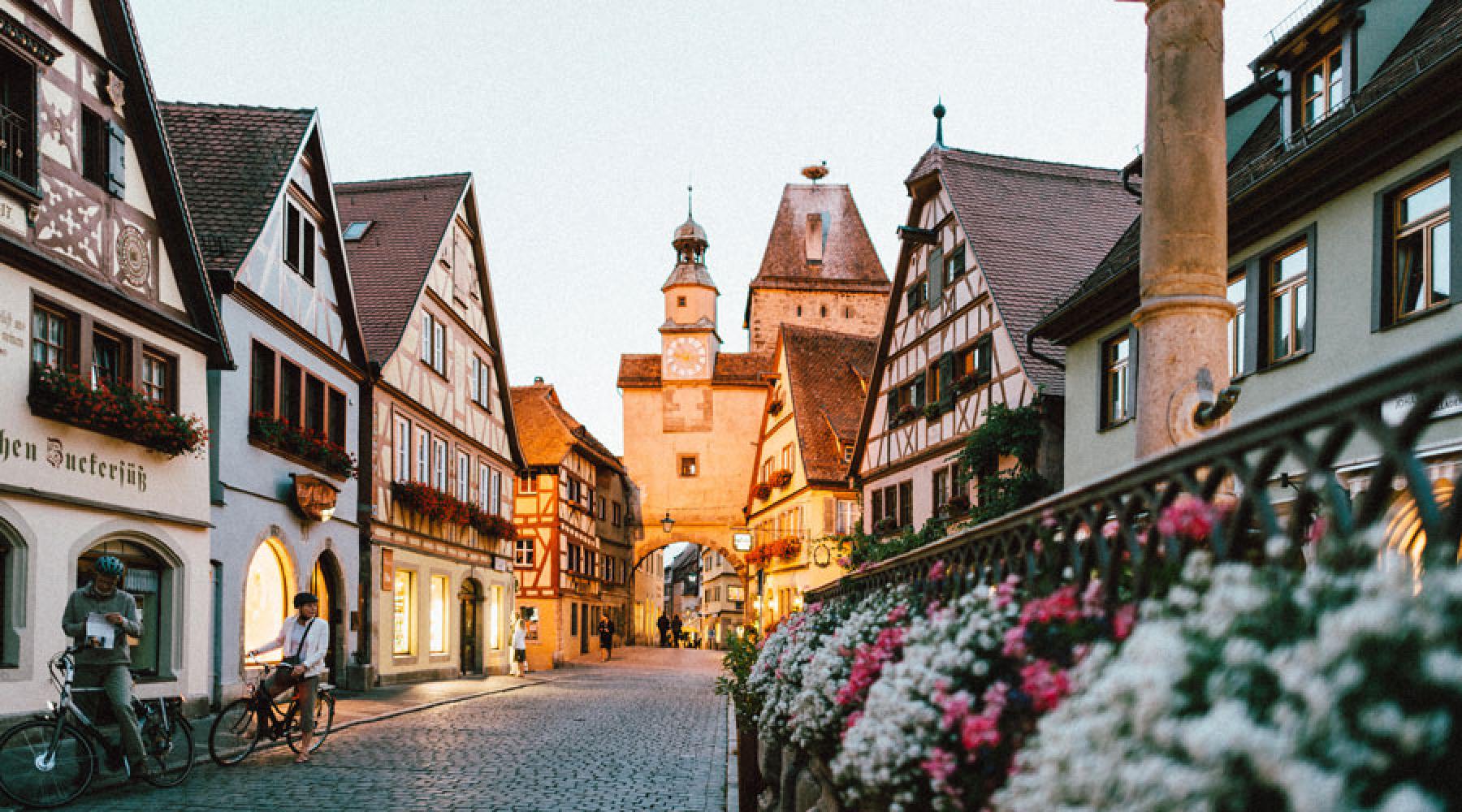 En gata i staden Rothenburg ob der Tauber: gamla korsvirkeshus och blommor, i bakgrunden en gammal stadsport med torn.
