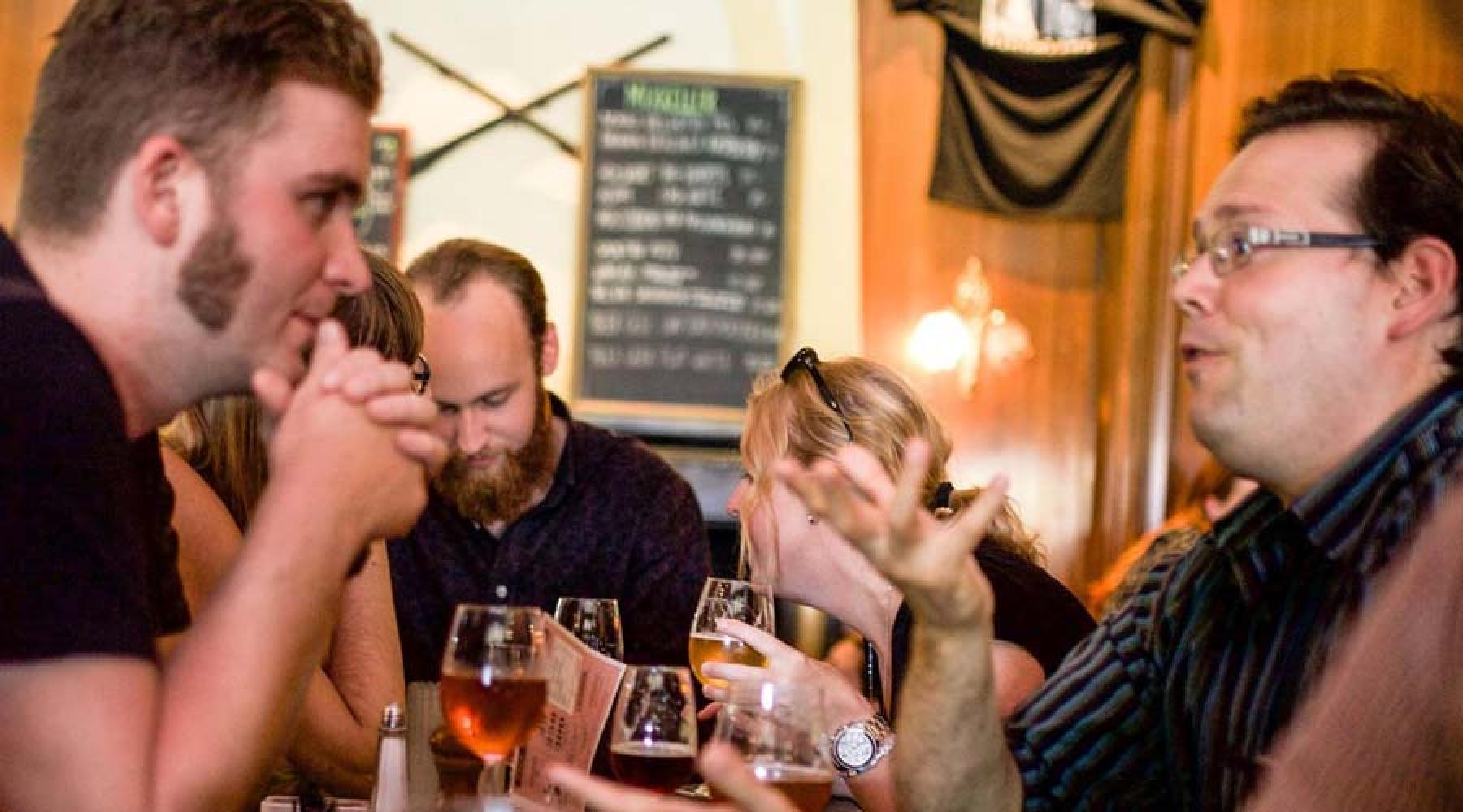 En grupp människor sitter på en pub, dricker öl och pratar med varandra.