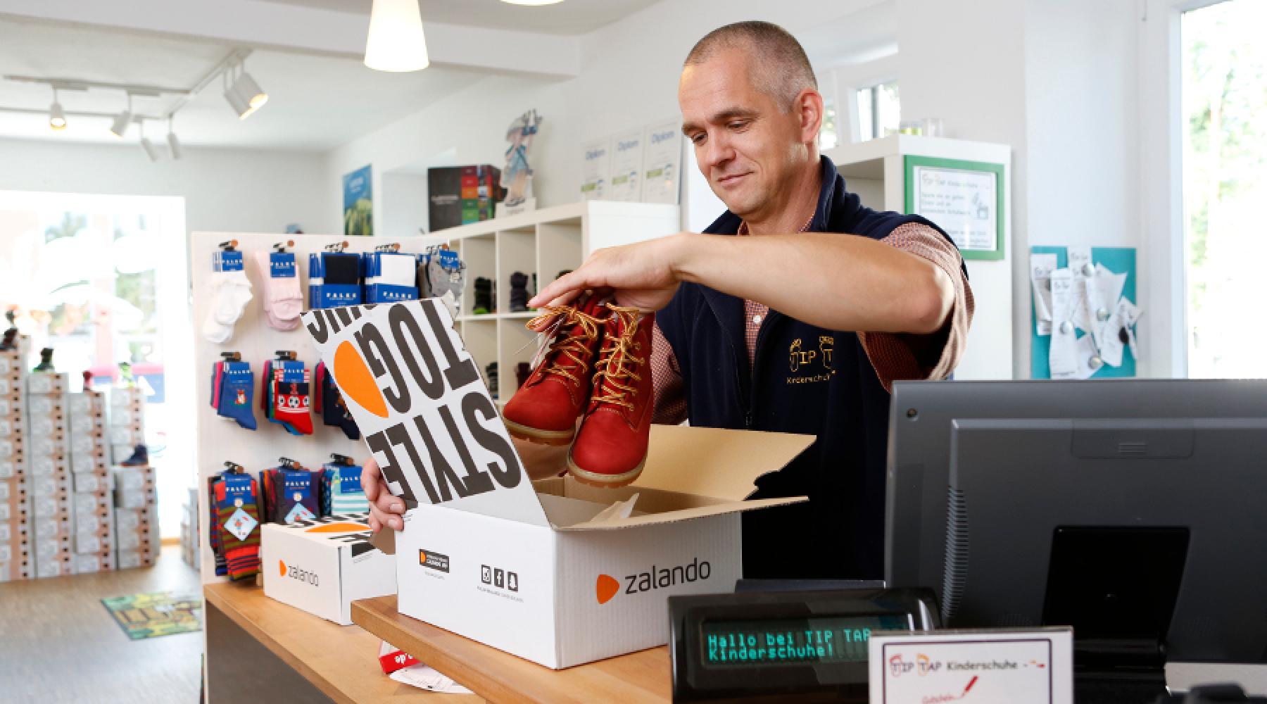 Ein Kassierer, der an einer Kasse ein paar Schuhe in einen Zalando-Karton packt.