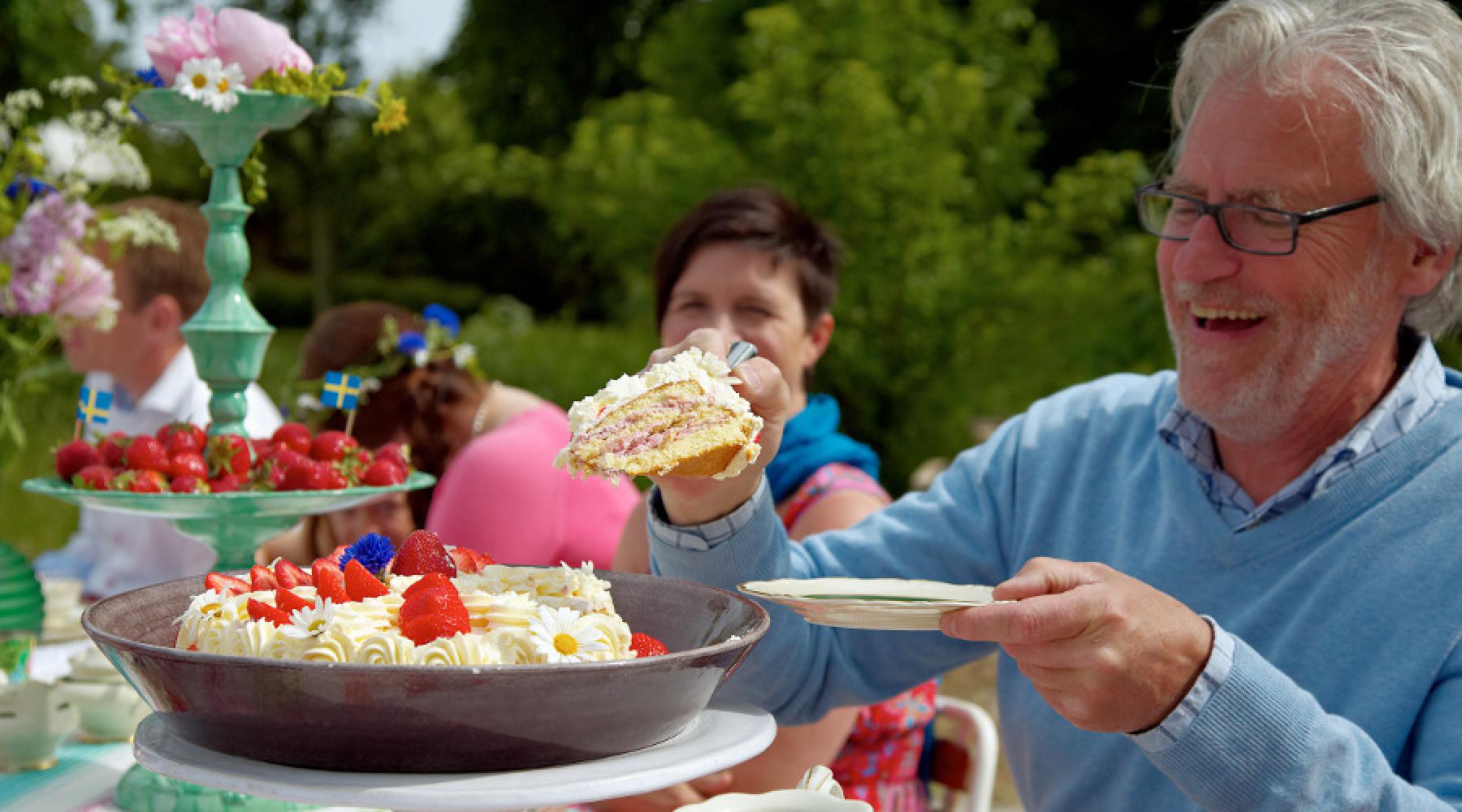 Ein Mann, der sich ein Stück Torte nimmt und dabei lacht.