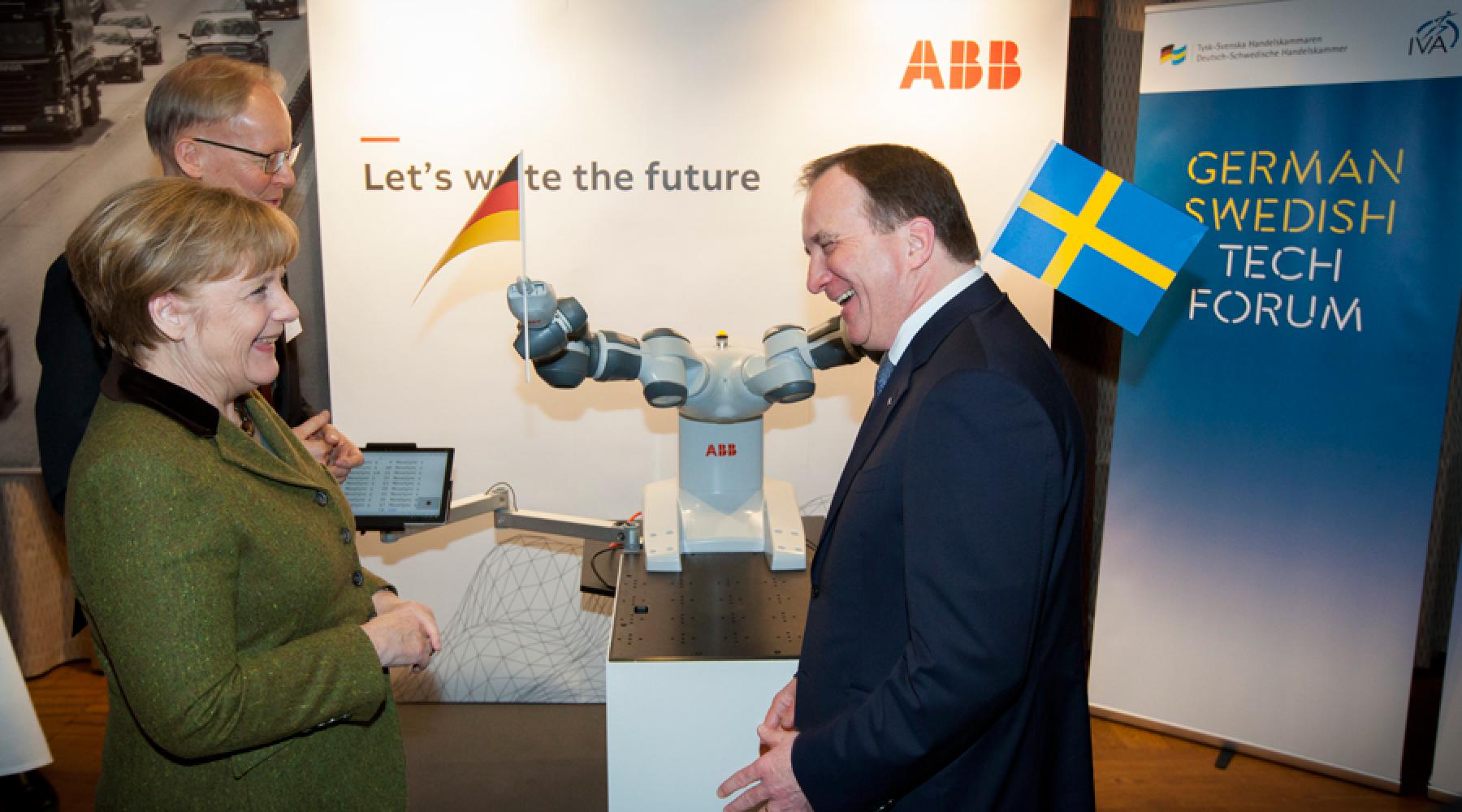 Bundeskanzlerin Angela Merkel und Schwedens Ministerpräsident Stefan Löfven vor einem ABB-Roboter mit je einer deutschen und einer schwedischen Fahne in den Greifarmen