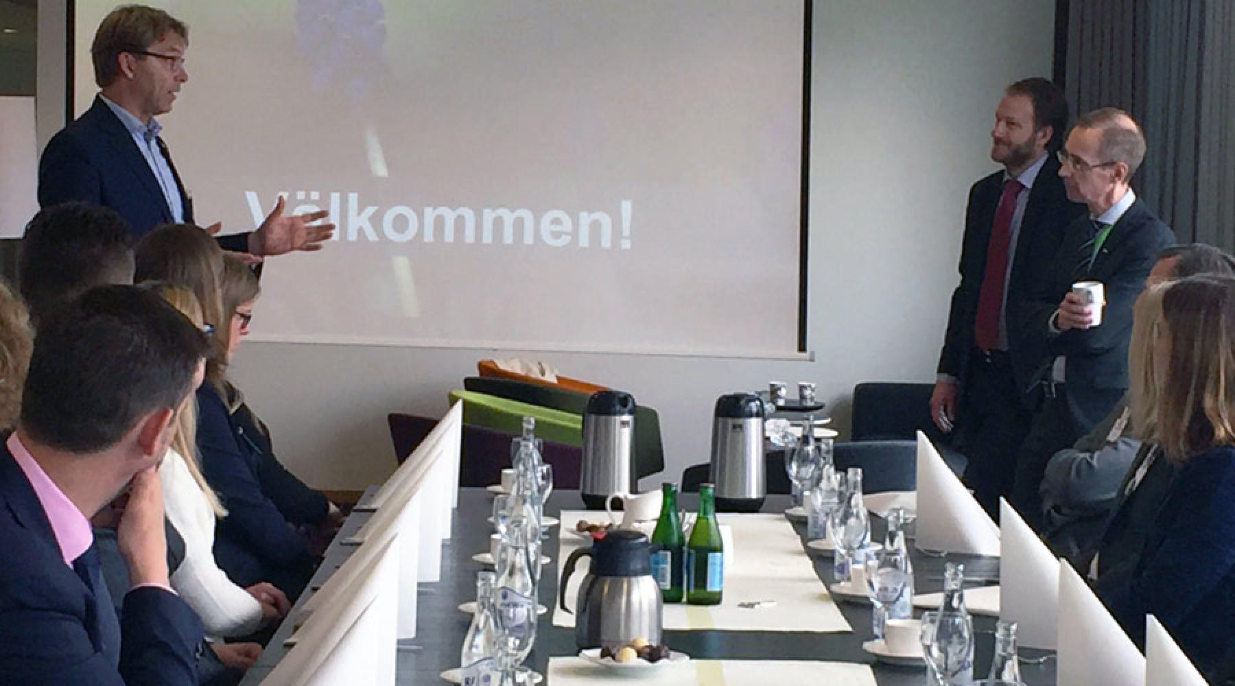 Ulf Troedsson står vid ena sidan av ett långt bord och talar till Robert Bergqvist och Daniel Bergvall på andra sidan. Vid bordet sitter seminariedeltagare.