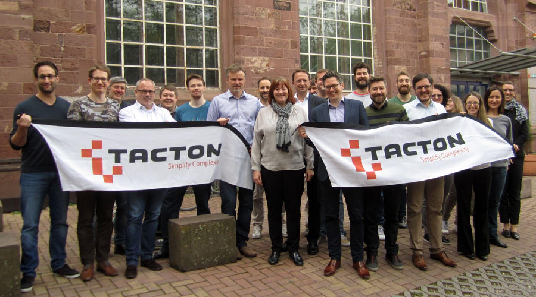 Gruppenfoto von Tactons Team in Karlsruhe mit zwei Tacton-Bannern in den Händen der Mitarbeiter