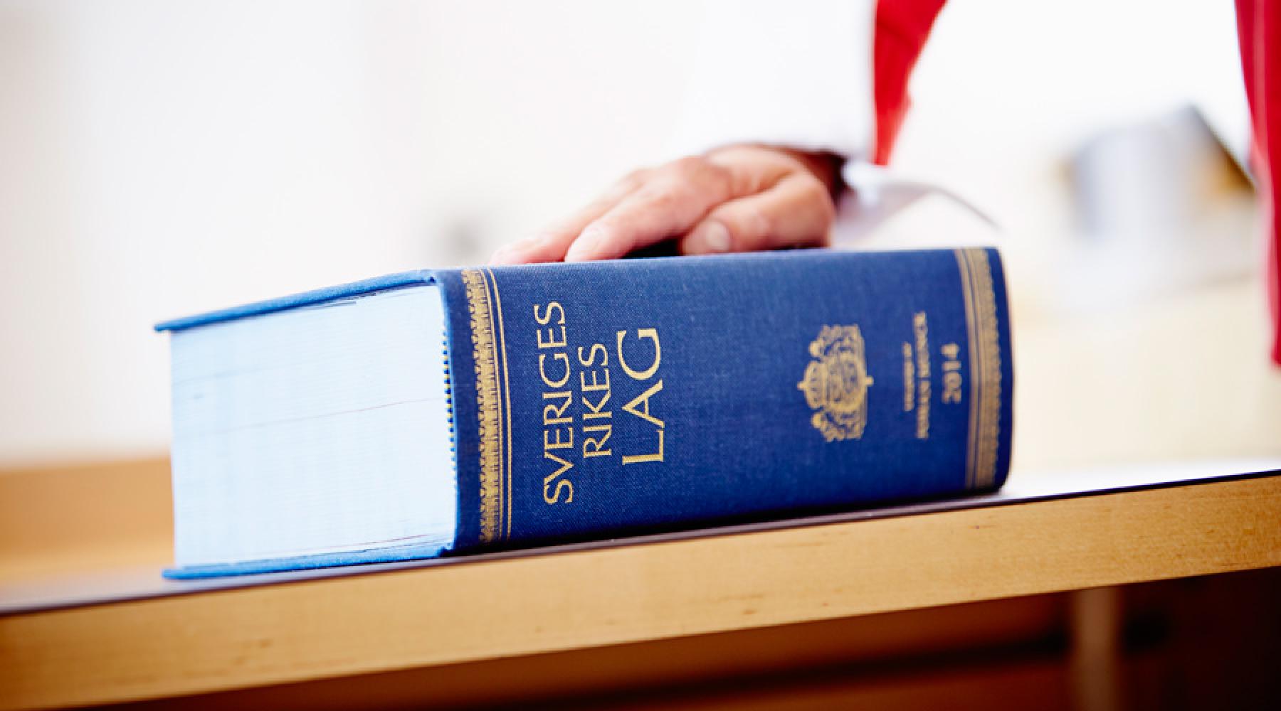 Lagboken "Sveriges rikes lag" ligger på ett bord.