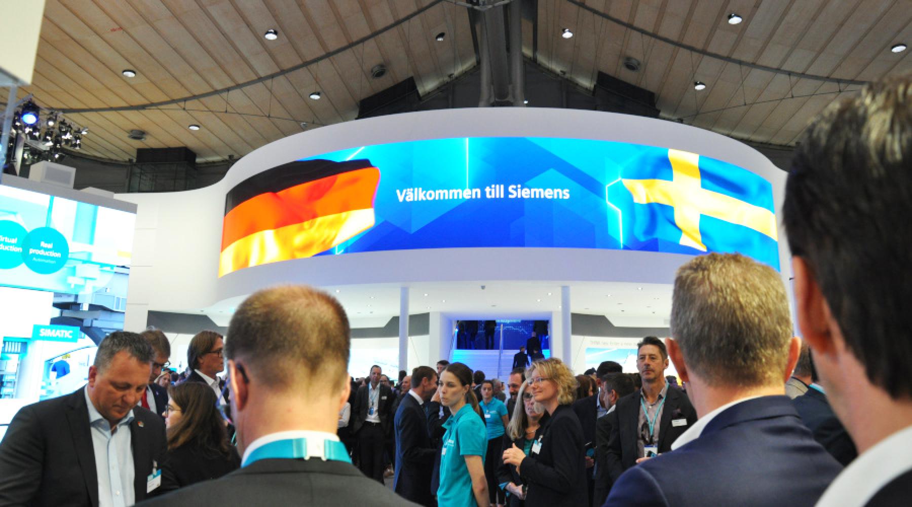 Siemens monter på Hannover Messe 2019: En stor skärm visar en tysk och en svensk flagga samt texten "Välkommen till Siemens".