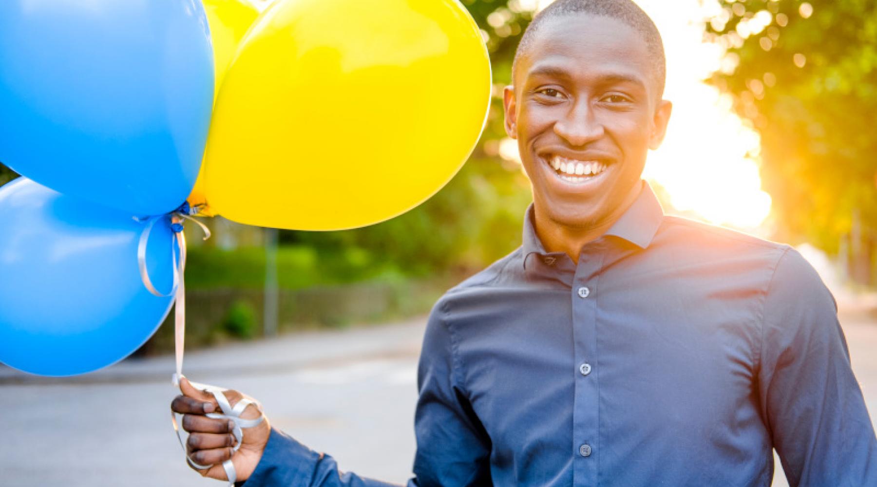 Ein Mann hält drei Luftballons in den schwedischen Nationalfarben blau und gelb in der Hand.