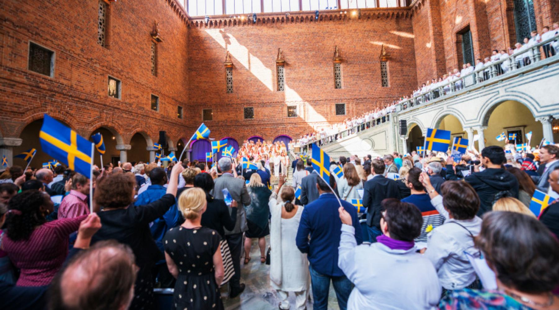 Die Blaue Halle im Stockholmer Rathaus mit vielen Besuchern und schwedischen Flaggen bei einer Zeremonie anlässlich des schwedischen Nationaltags