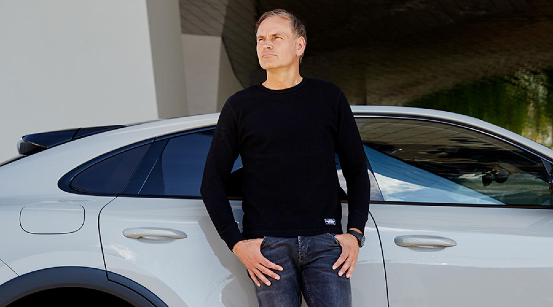 Porsches vd Oliver Blume lutandes mot en Porsche-bil