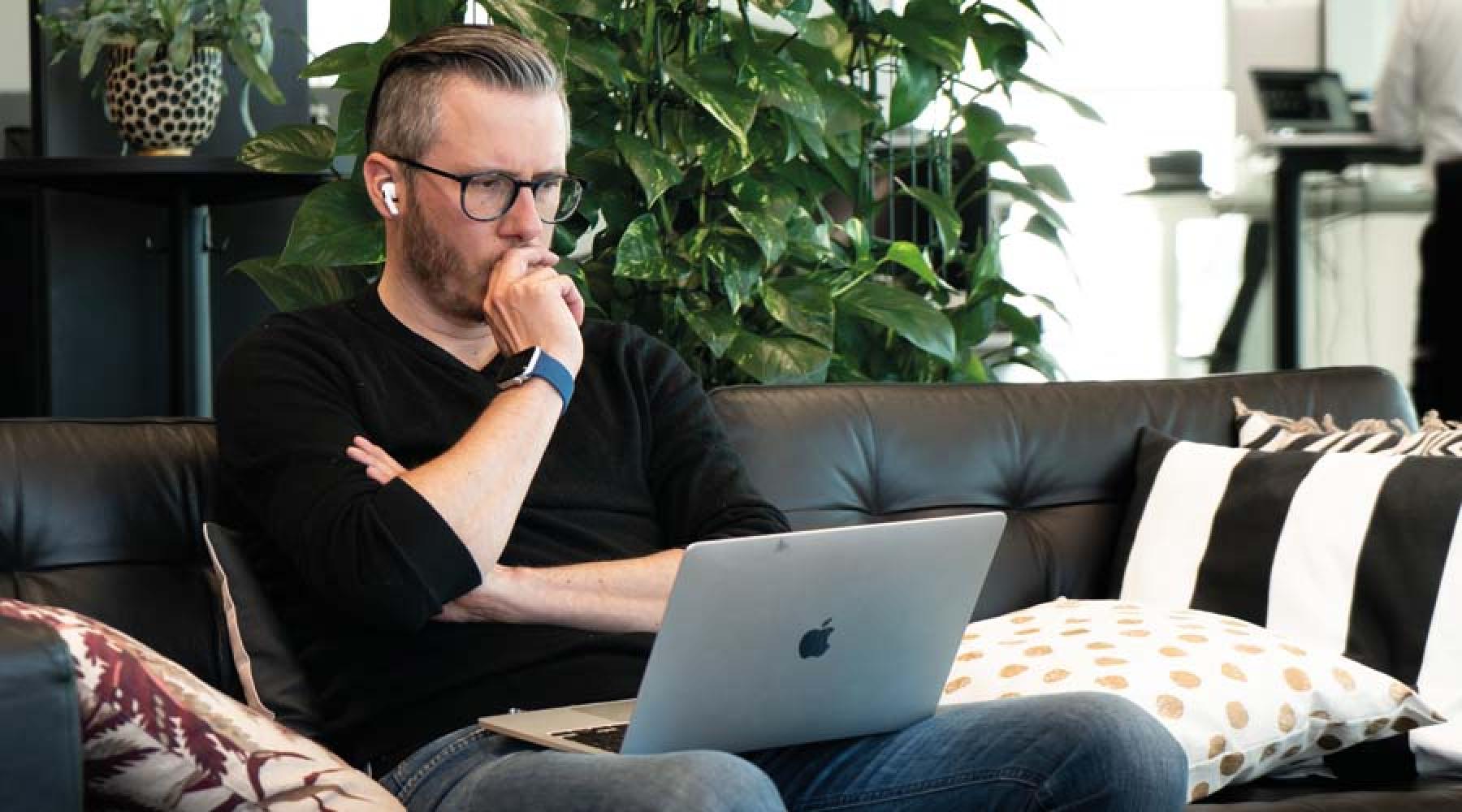 Ein Mann mit einem Computer auf dem Schoss auf einer Couch