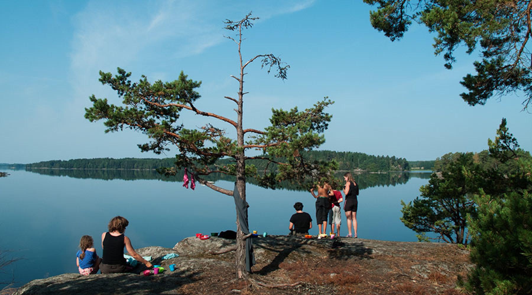 Vuxna och barn sitter på en klippa vid spegelblank sjö