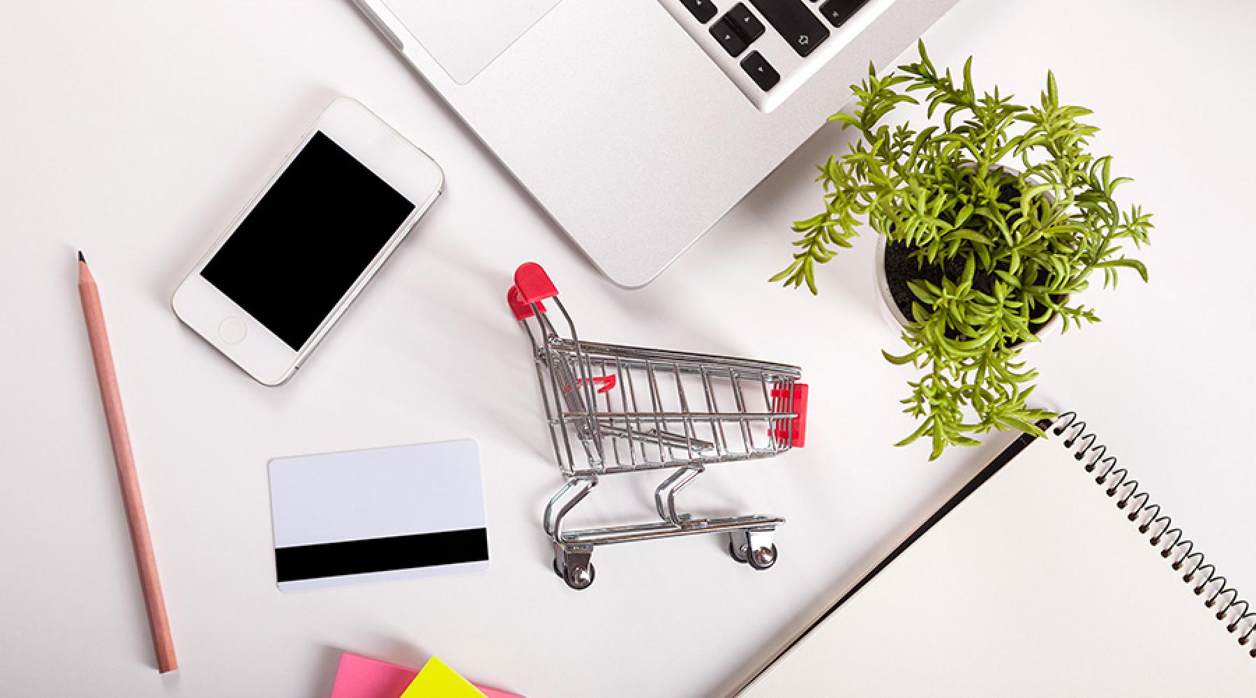 En bild på en dator, mobiltelefon och en miniatyrkundvagn